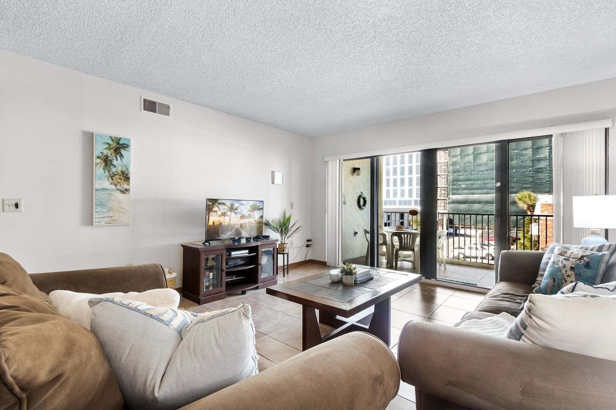 A living room with a TV, sofa, and a balcony with a view.