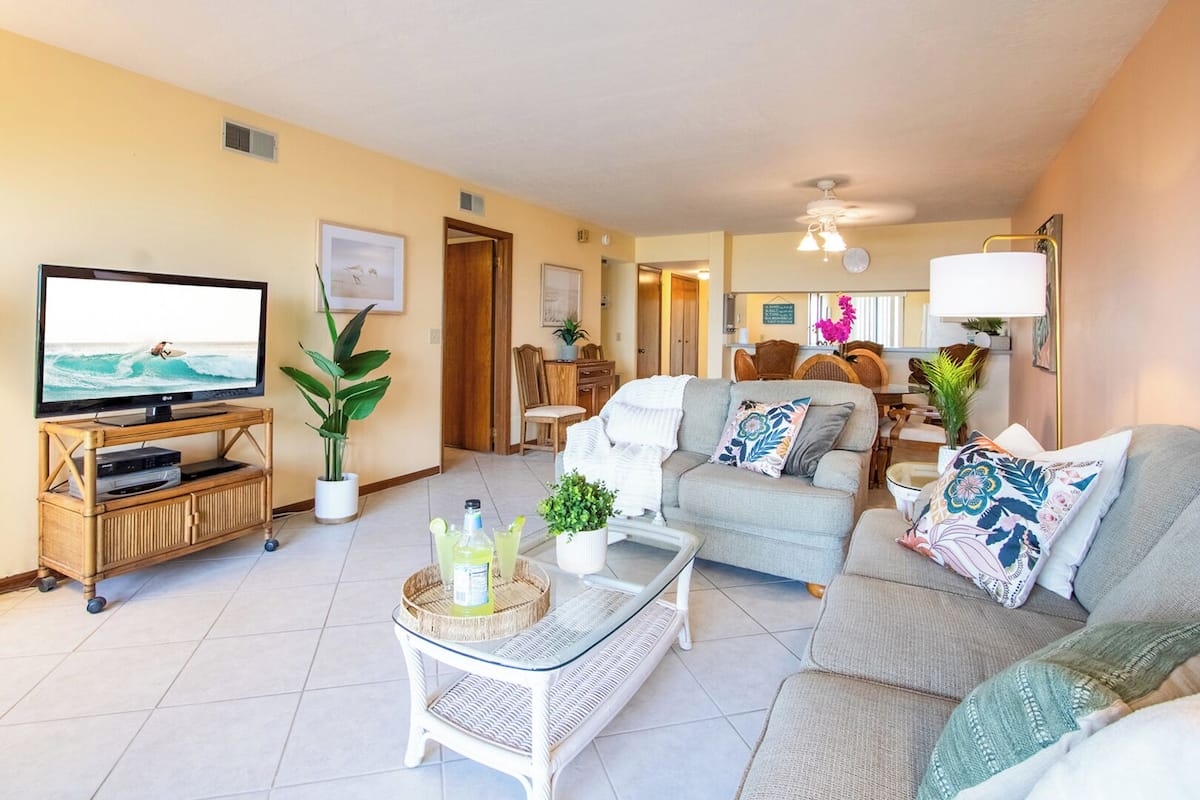 A living room with a TV, sofa, coffee table, and a dining area with chairs and a table.