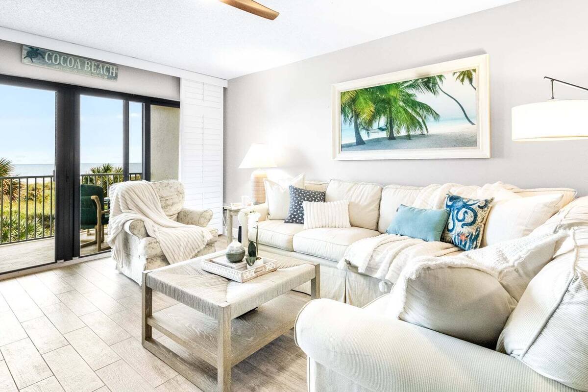 A living room with a sofa, armchairs, a coffee table, and a painting of a beach scene.