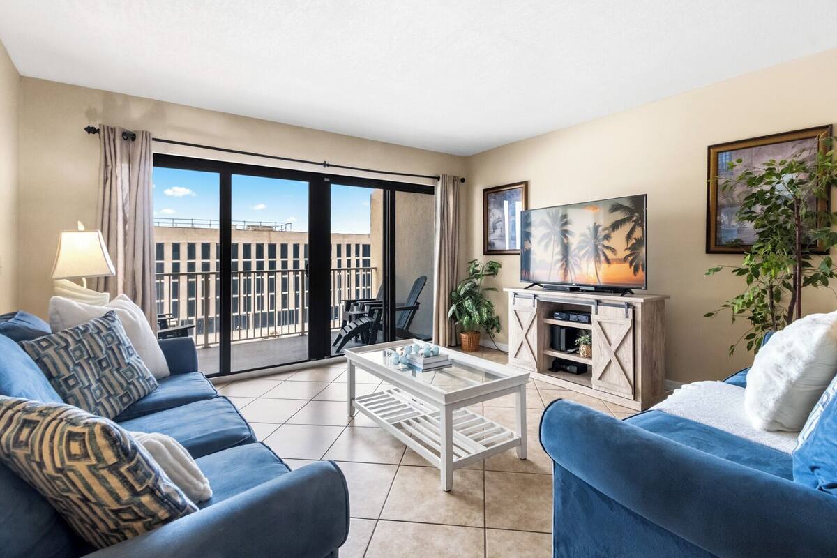 A living room with a sofa, coffee table, TV, and a balcony with a city view.