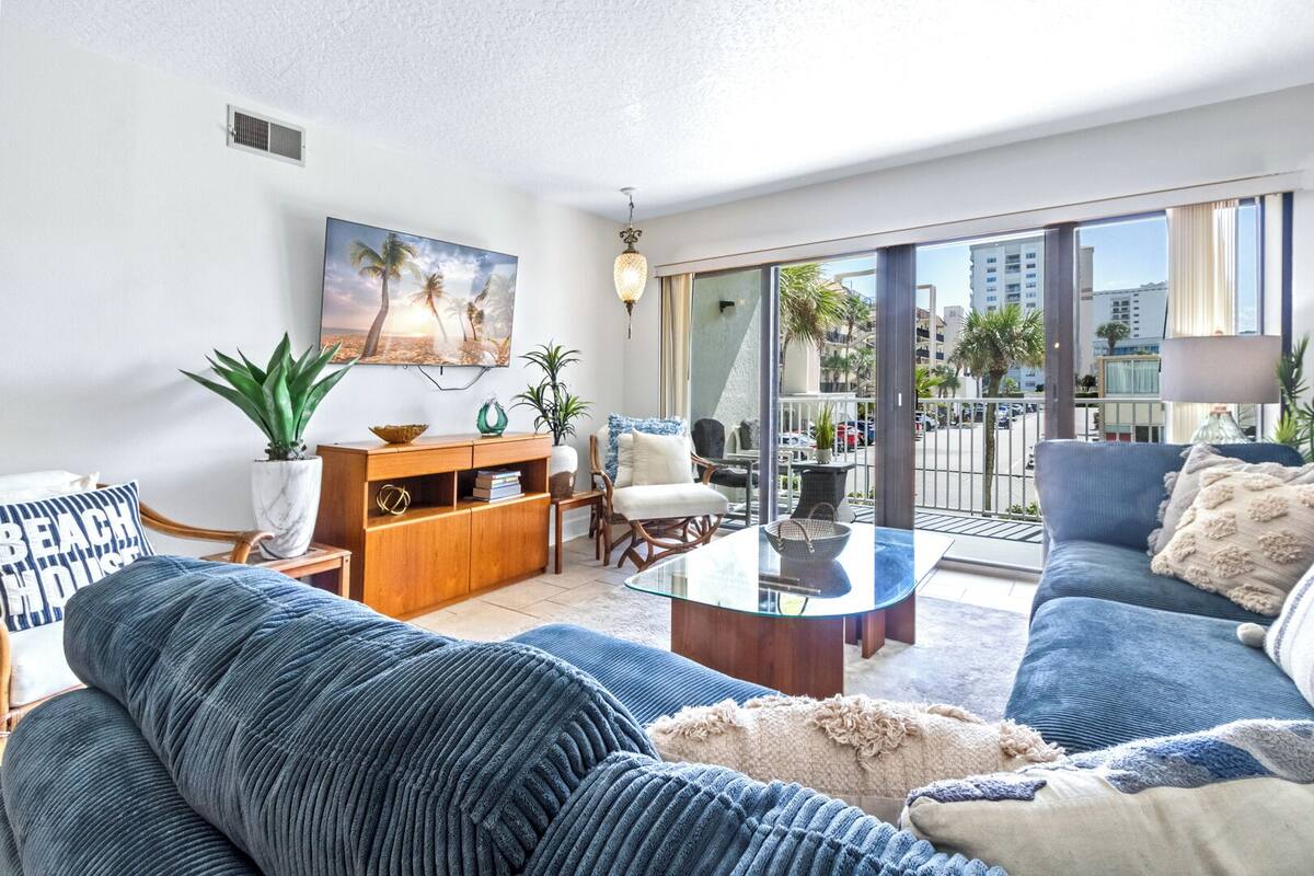 A modern living room with a sofa, coffee table, and a view of the city through large windows.