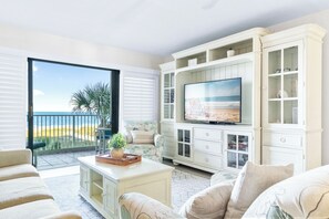 A spacious living room with a large TV, white cabinetry, and a balcony with a view of the beach. - Sandcastles - Cocoa Beach Oceanfront Condos with Heated Pool Tennis Pet-Friendly (Cocoa Beach)