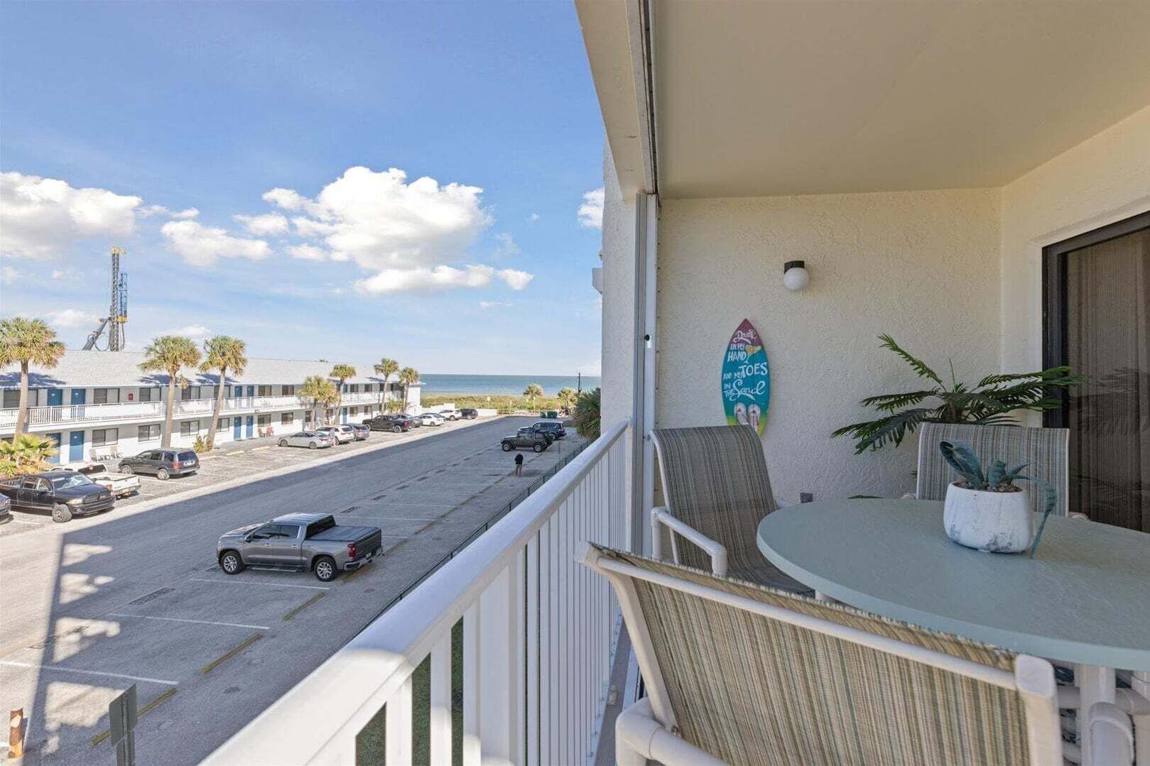A balcony with a view of a street, a surfboard, and a plant.