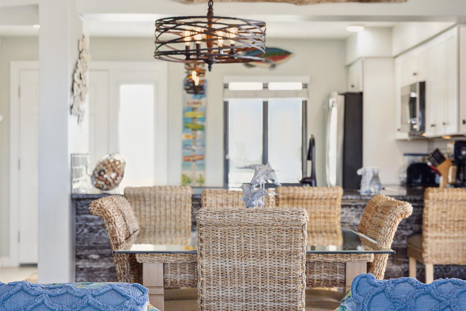 A dining area with wicker chairs, a glass table, and a hanging light fixture.