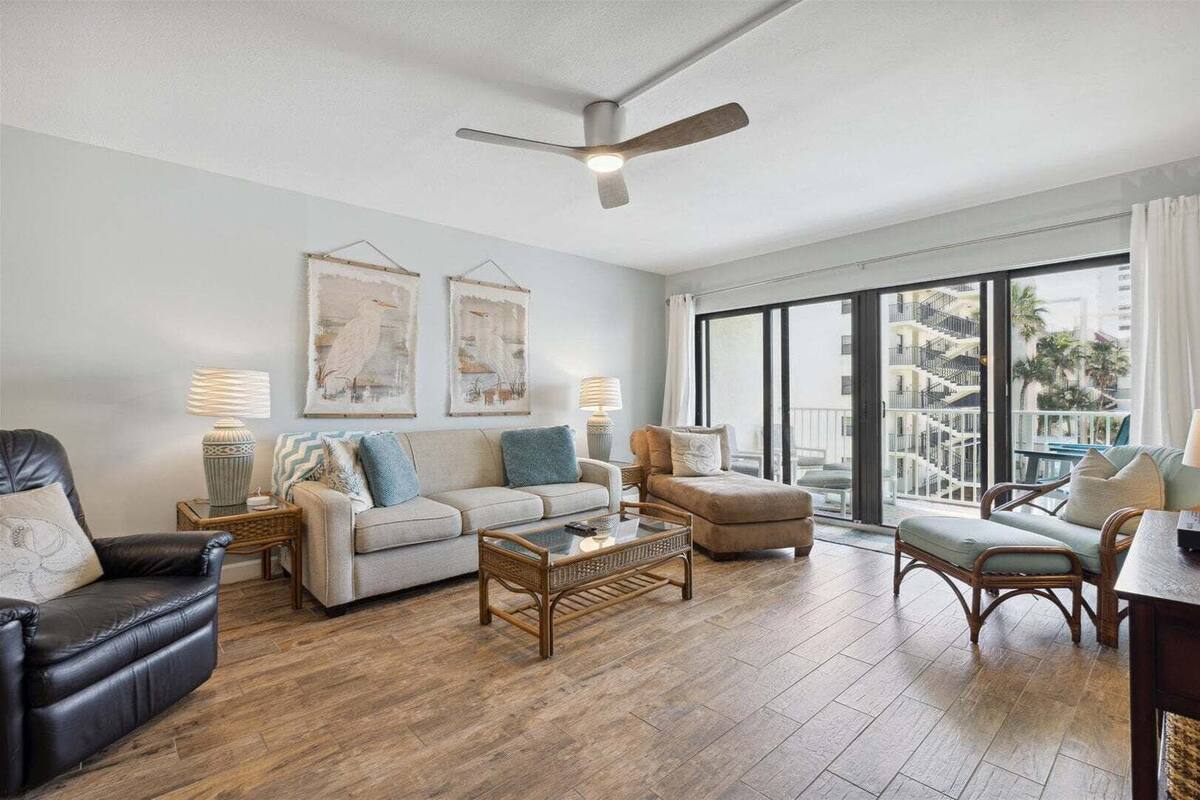 A spacious living room with a sofa, armchairs, a coffee table, and a ceiling fan.