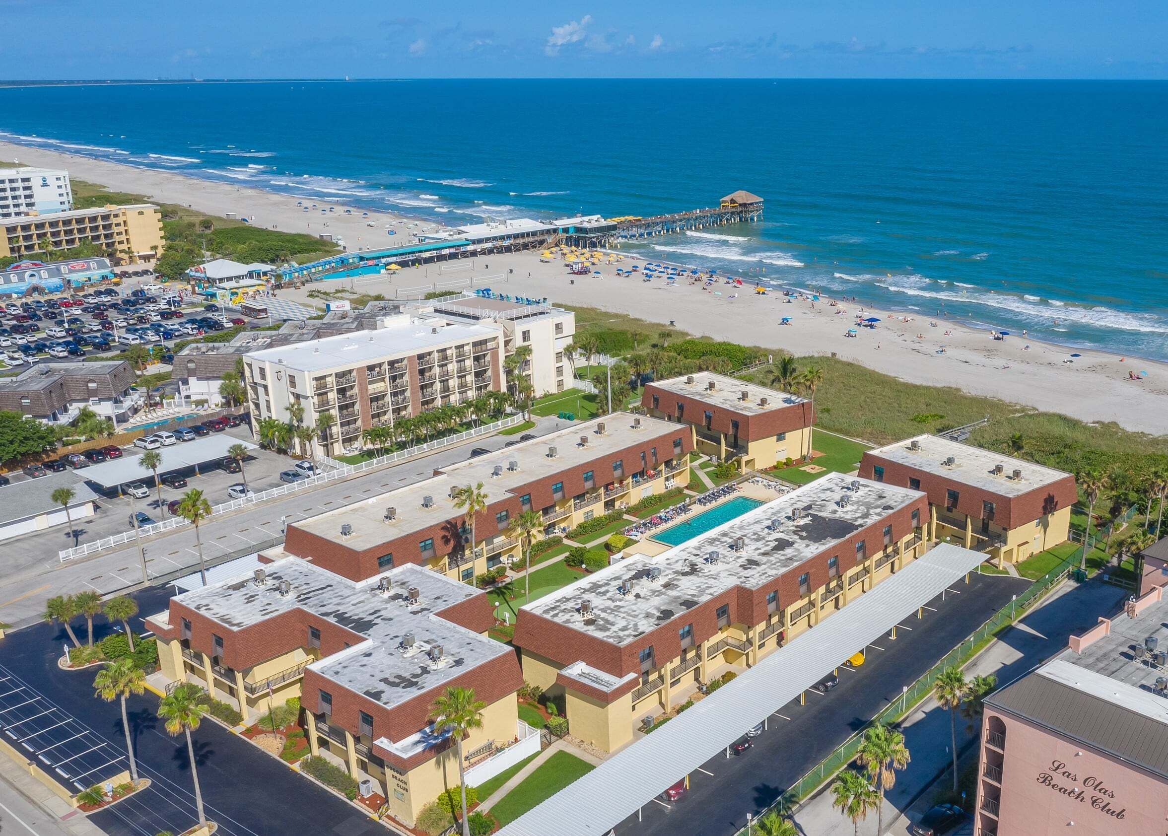 Een strandhotel met meerdere gebouwen, een zwembad en een pier die in de oceaan uitloopt.