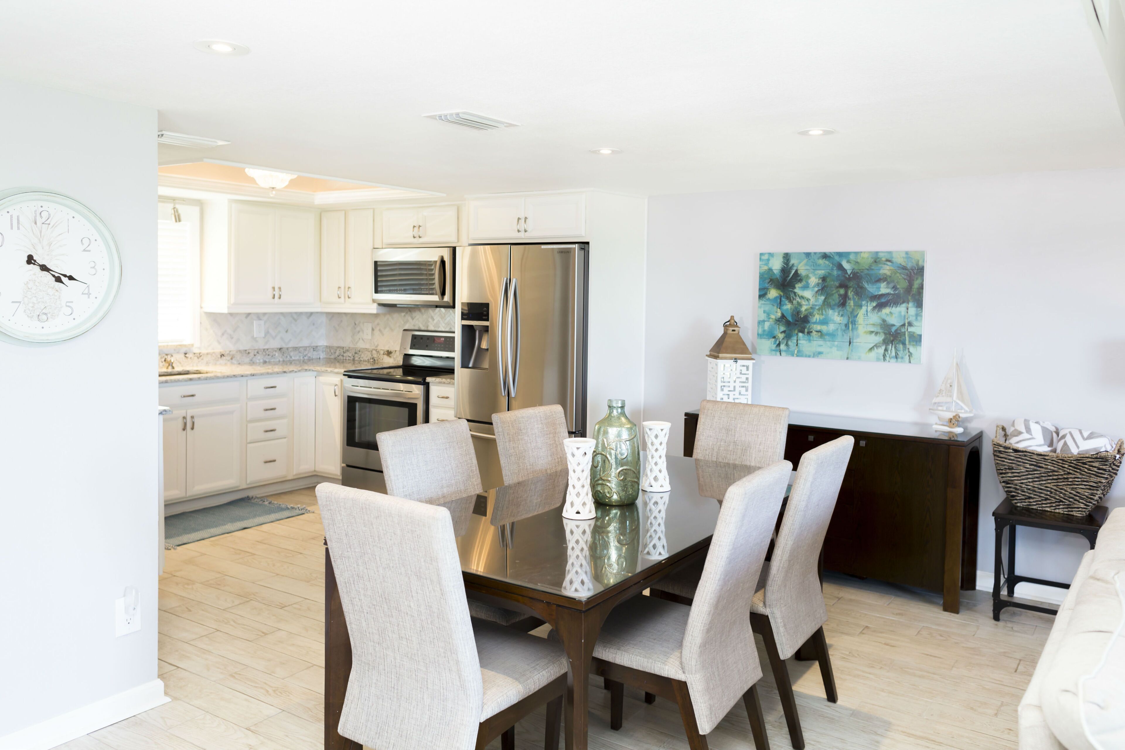 Una cocina moderna con gabinetes blancos, electrodomésticos de acero inoxidable y un comedor con mesa y sillas de vidrio.