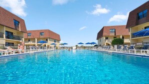 Una piscina con sillas de descanso y sombrillas, rodeada de edificios de varios pisos con balcones.