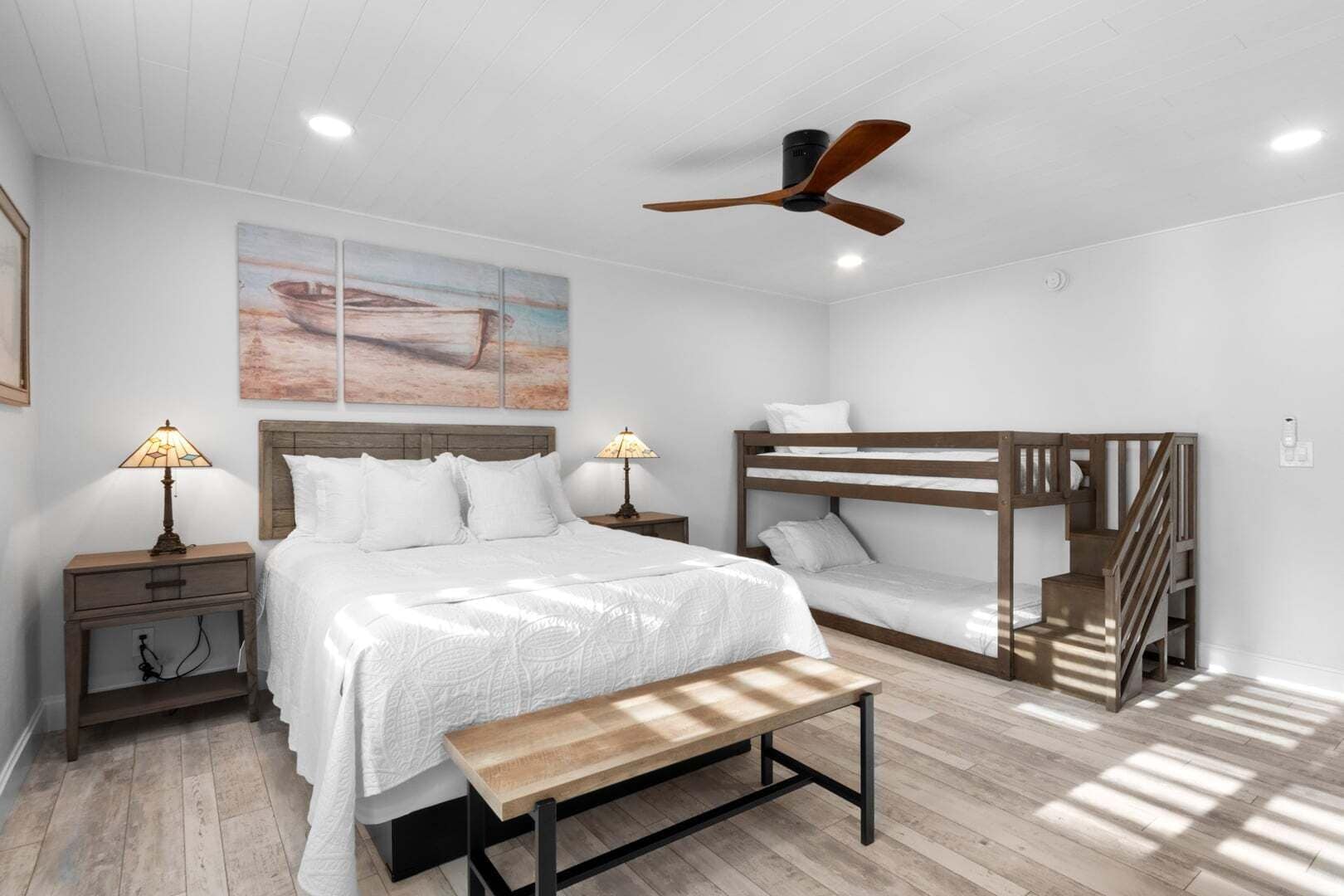 Una camera da letto con un letto a castello, una panca in legno, due comodini con lampade e un ventilatore a soffitto, oltre a un quadro appeso al muro.