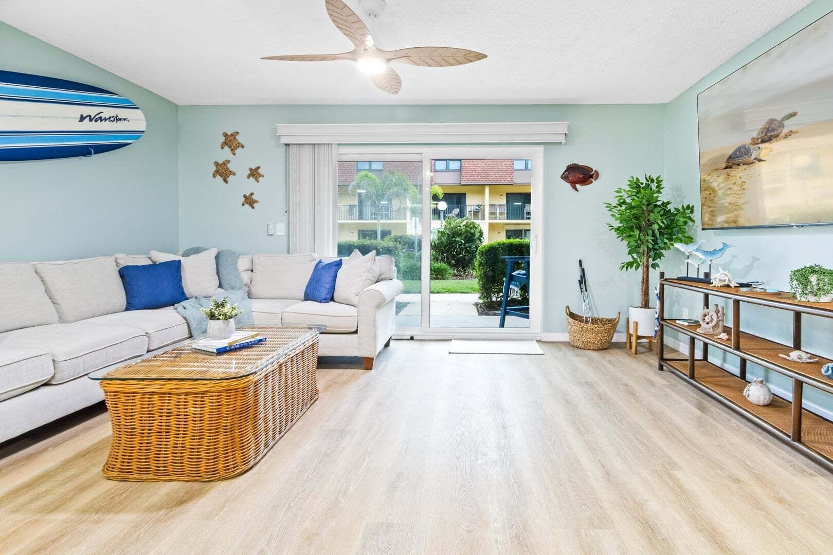 A modern living room with a sofa, a wicker coffee table, a ceiling fan, and a sliding glass door leading to an outdoor area.