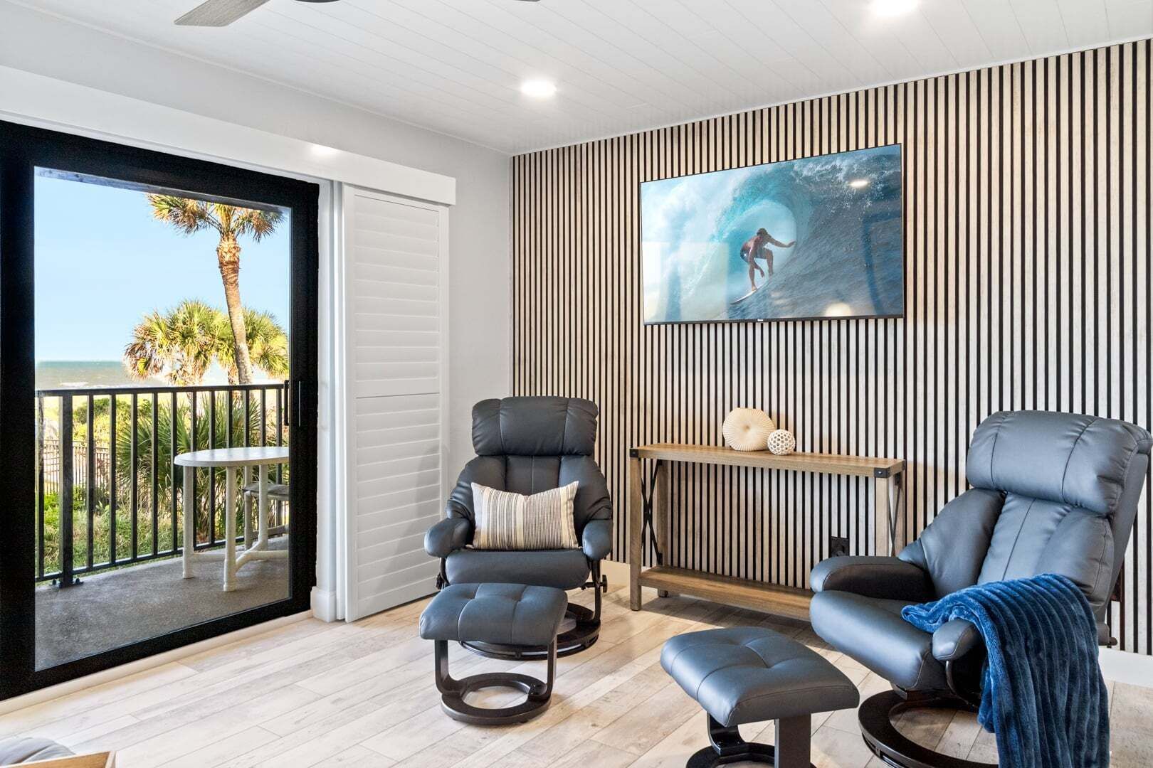 A modern living room with two reclining chairs, a small table, and a large TV on a wall with vertical stripes.