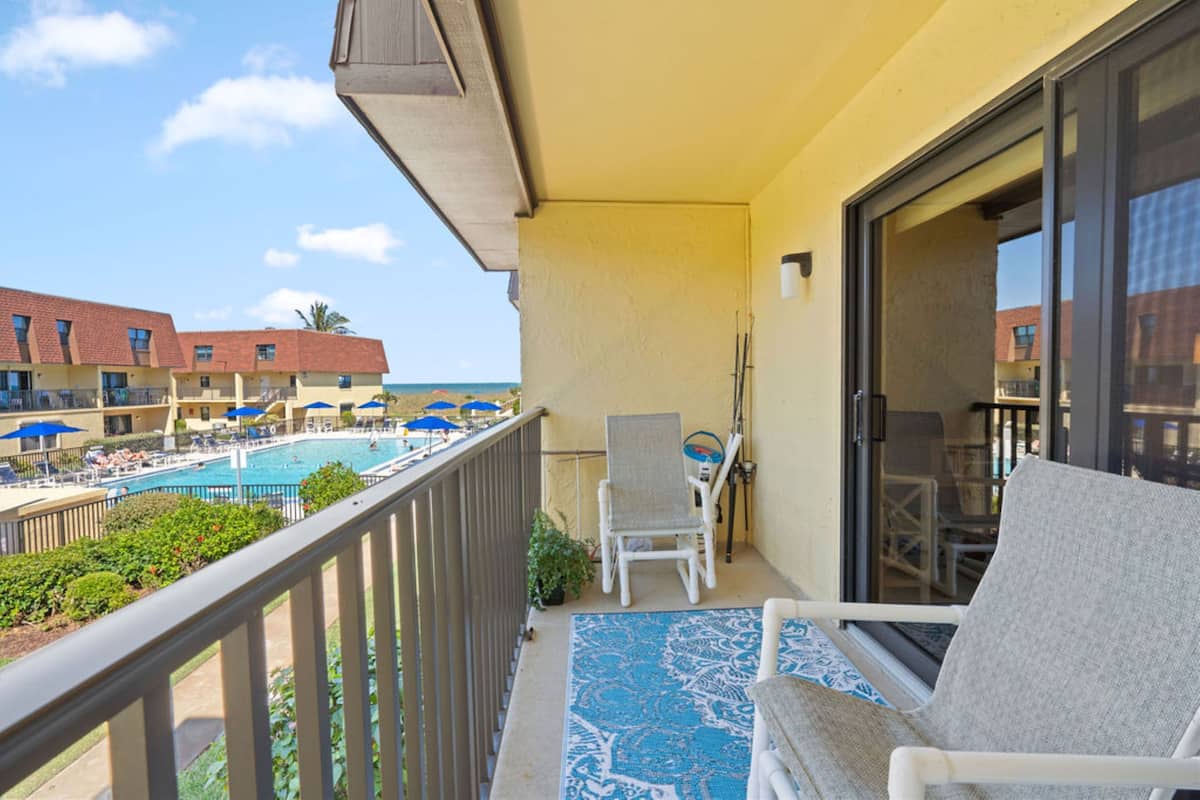 Un balcó amb vista a la piscina, una cadira i una porta que dona a una altra habitació.