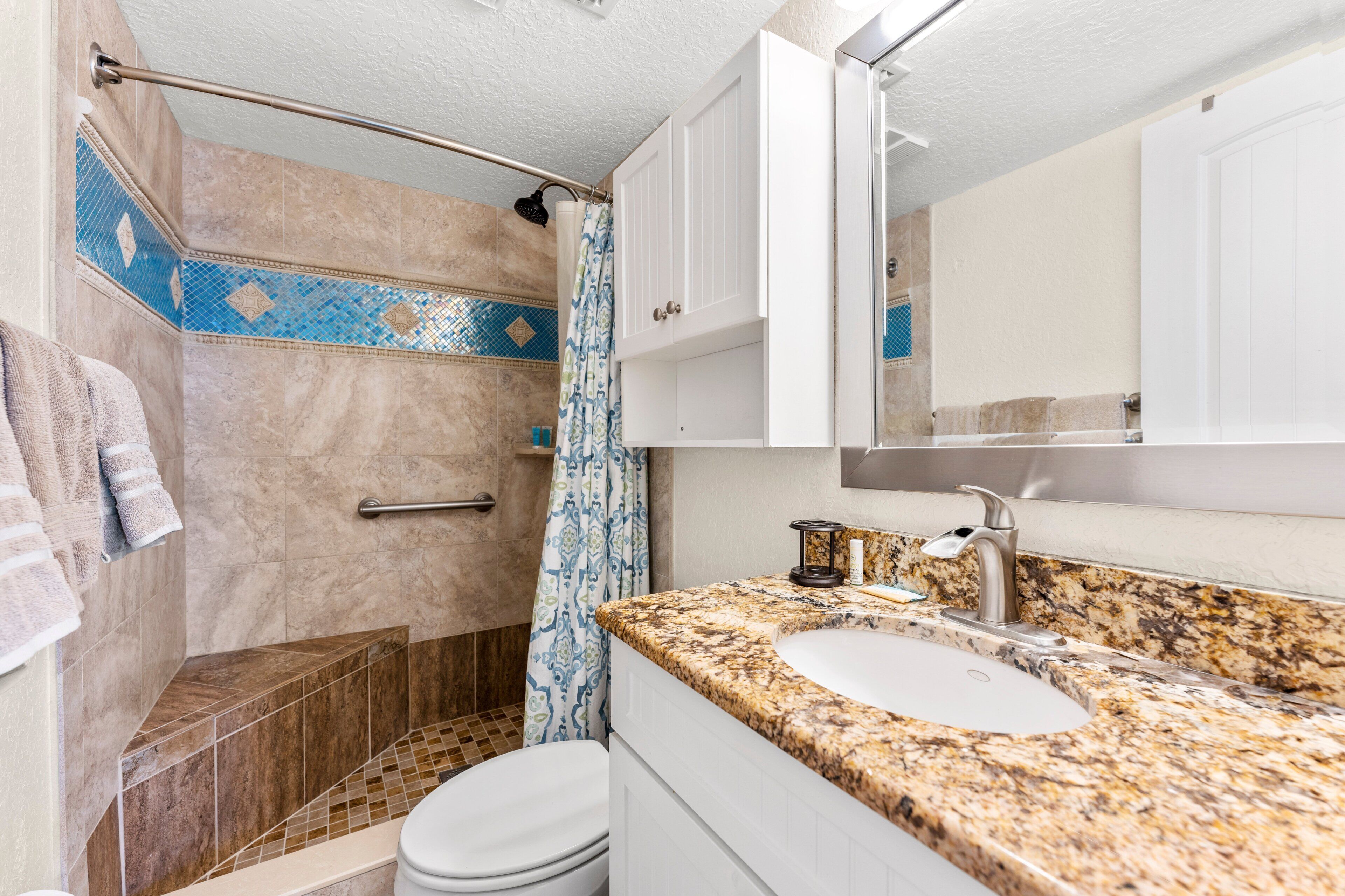 A bathroom with a shower, toilet, sink, and a mirror.