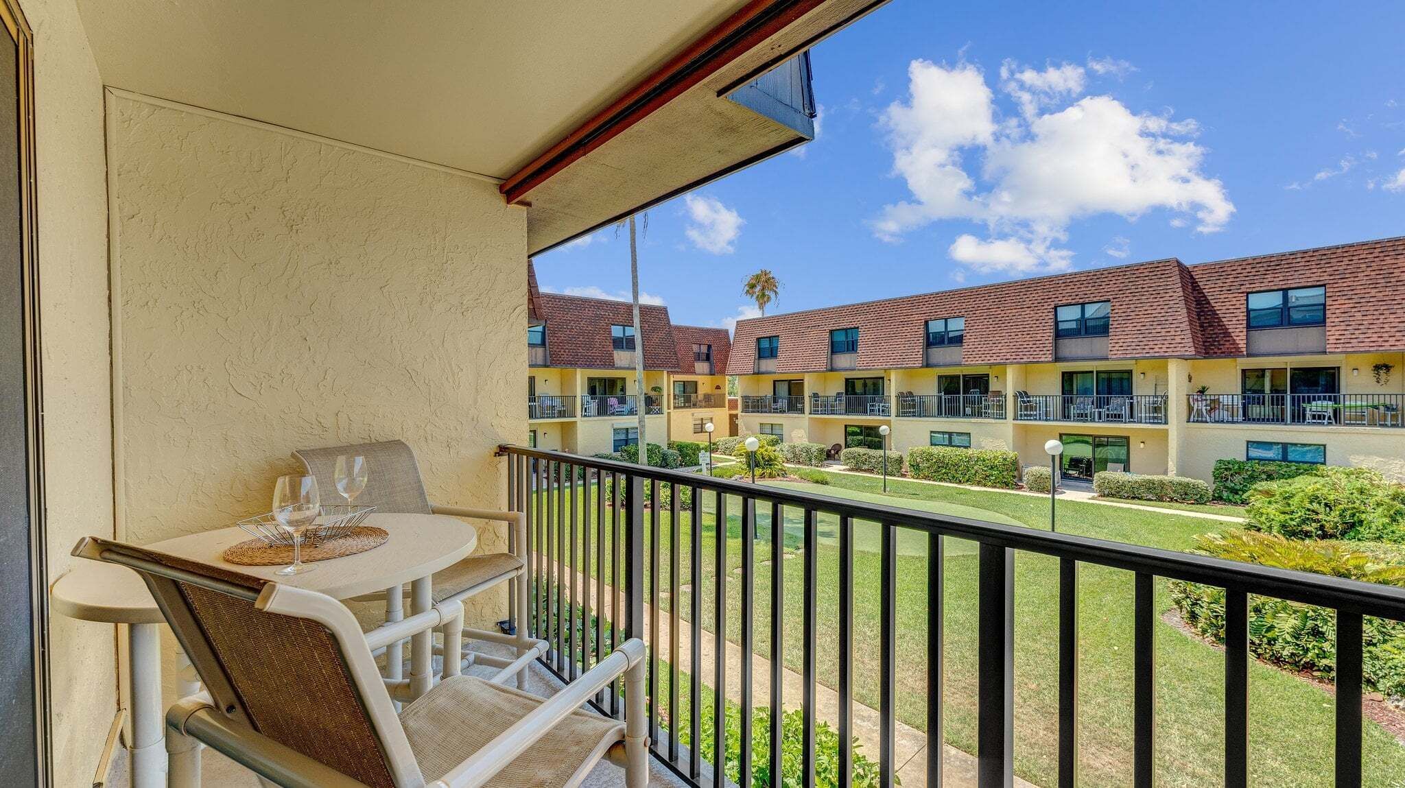 Un balcón con mesa y sillas, que da a un patio interior con un edificio al fondo.
