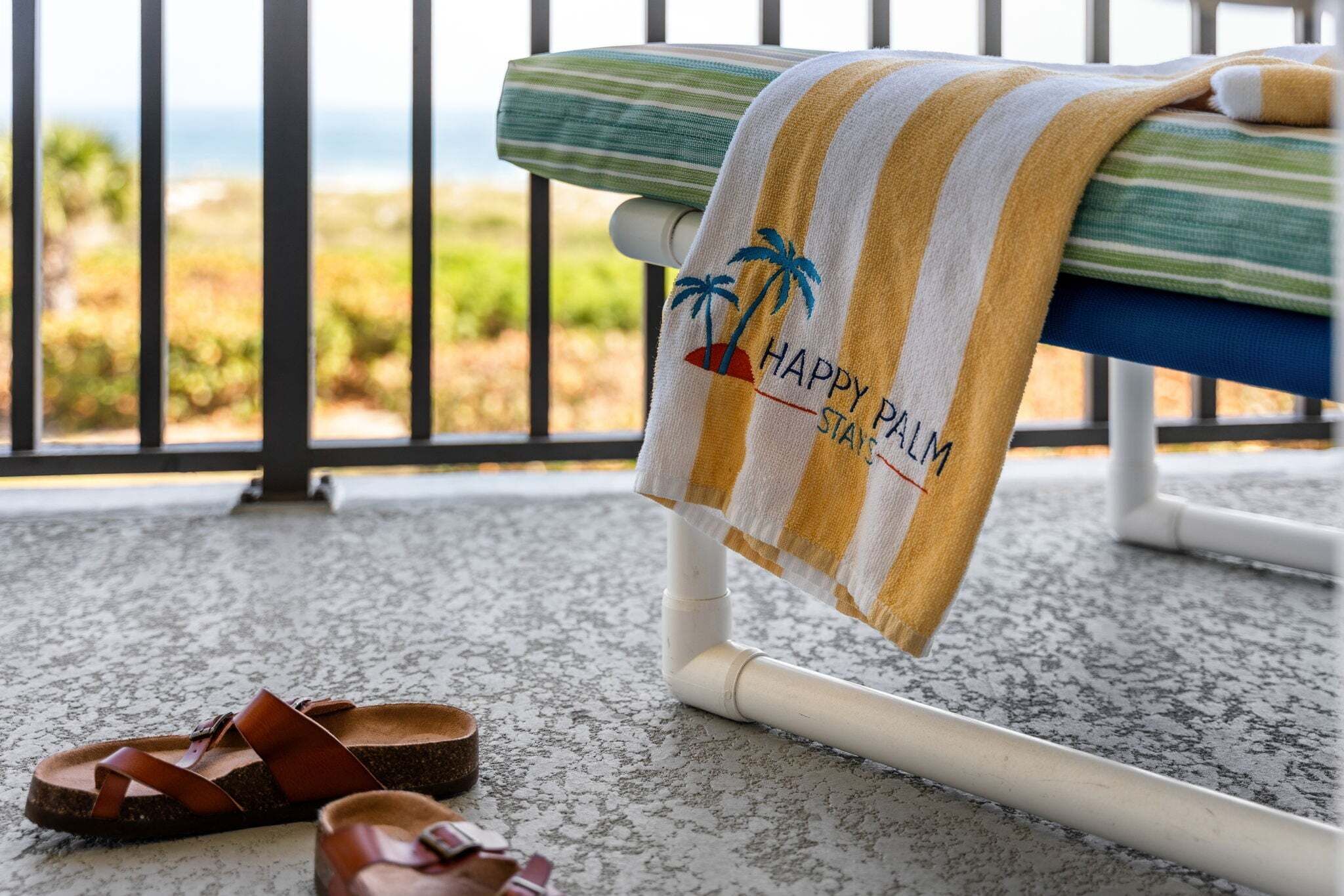 Un banco con una toalla echada, un par de sandalias en el suelo y vistas a la vegetación y un cuerpo de agua.