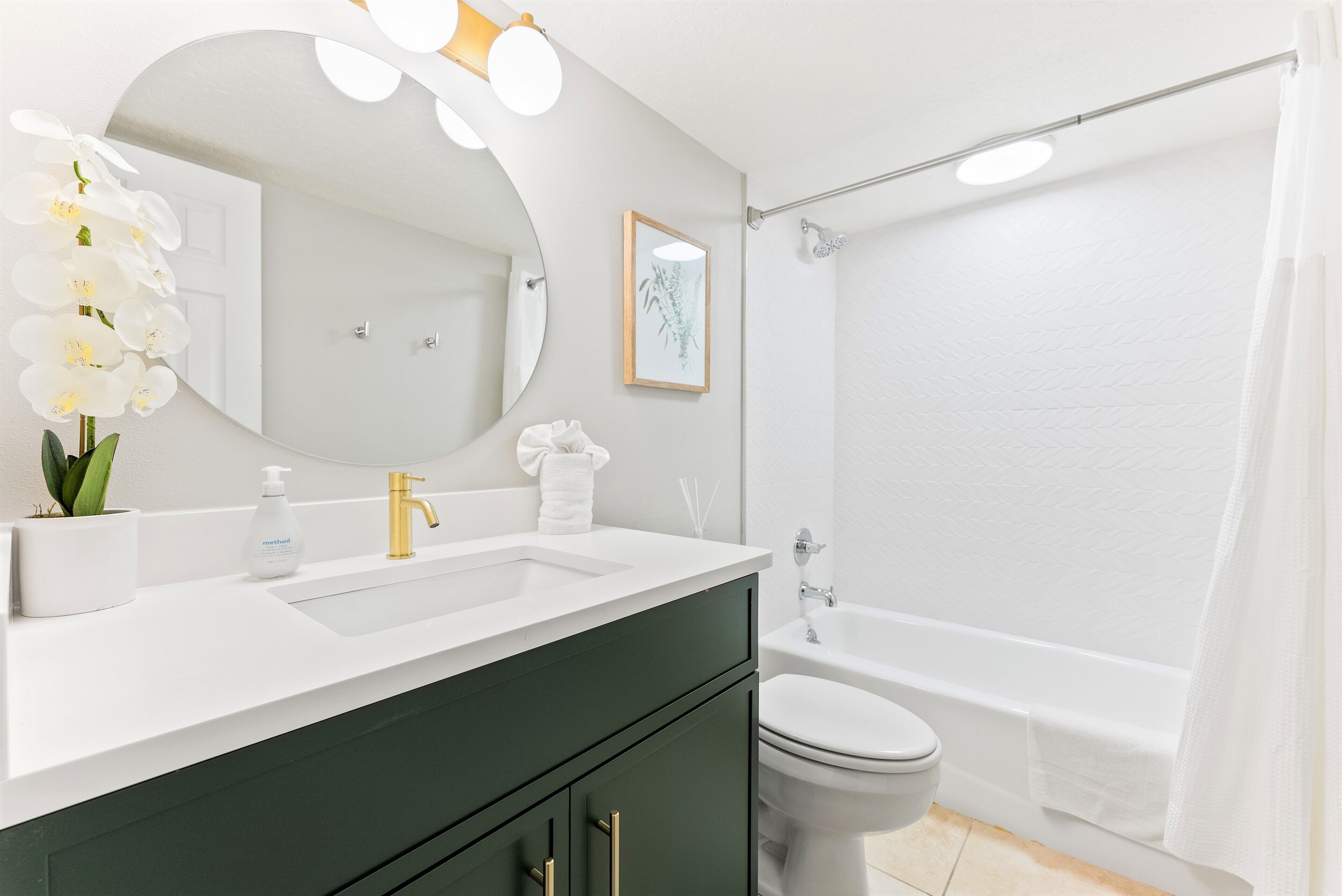 A modern bathroom with a white sink, green cabinets, a large mirror, and a bathtub.