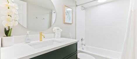 A modern bathroom with a white sink, green cabinets, a large mirror, and a bathtub.