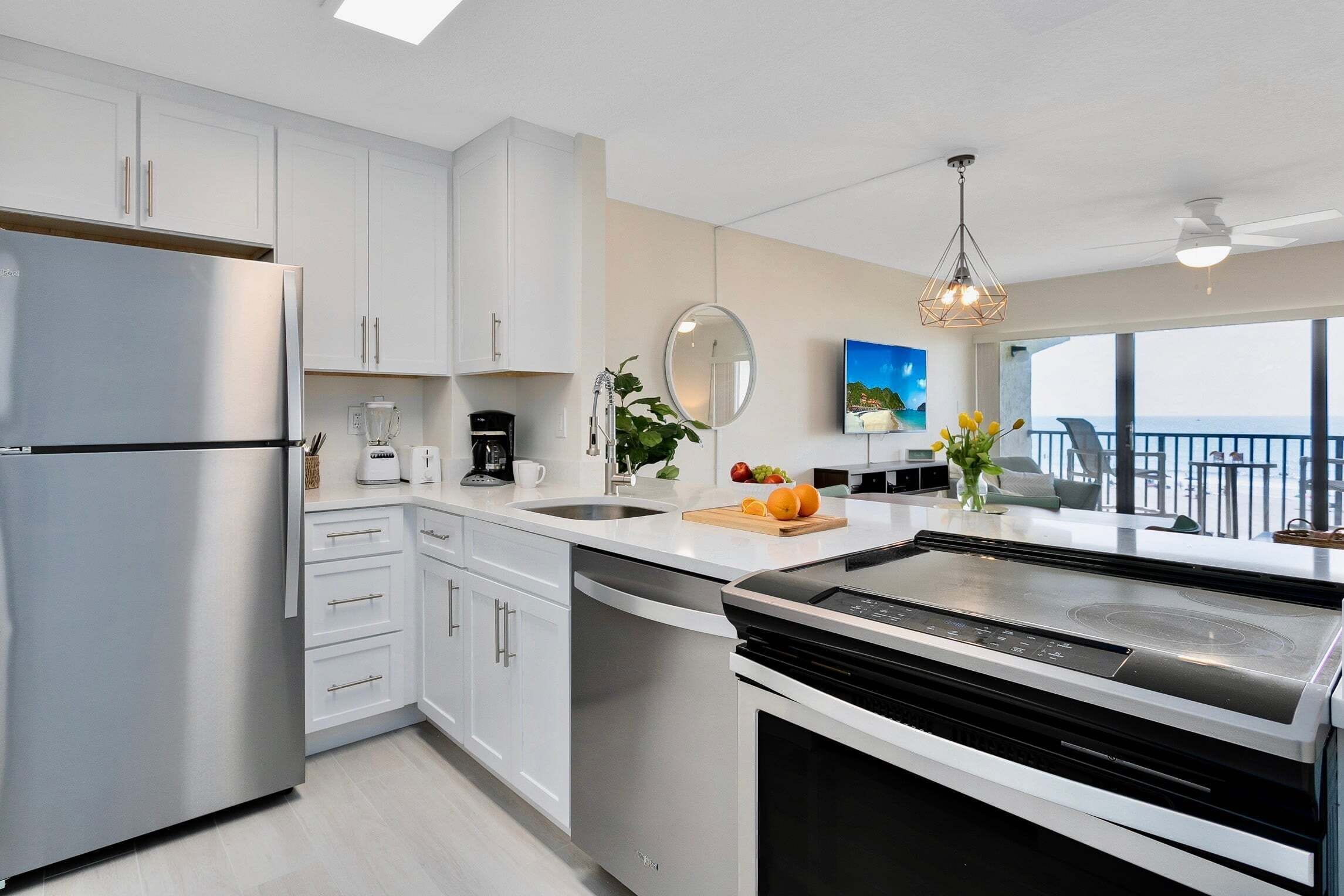 A modern kitchen with stainless steel appliances, white cabinetry, a large island, and a view of the ocean.