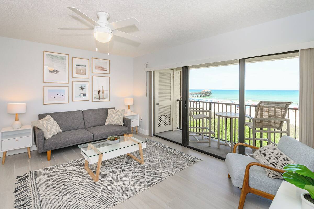 Un soggiorno moderno con un divano grigio, un tavolino in vetro e un balcone con vista sulla spiaggia.