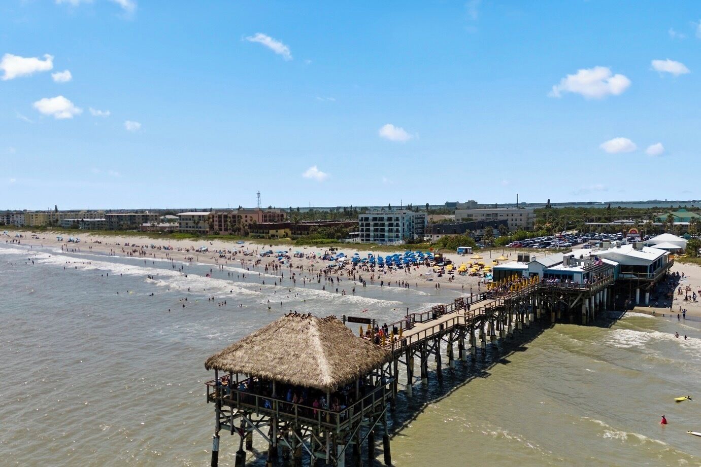 A beach with a pier, beach umbrellas, and a thatched-roof structure.