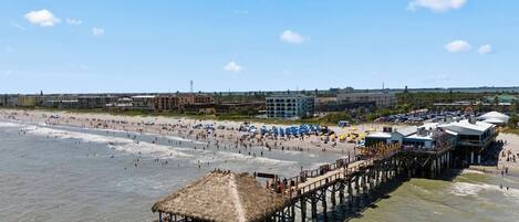 A beach with a pier, beach umbrellas, and a thatched-roof structure.
