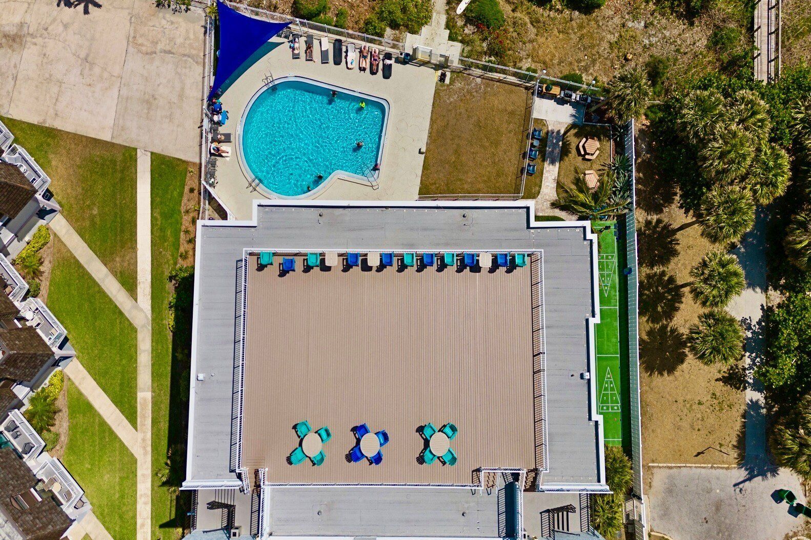 An aerial view of a hotel with a swimming pool, sun loungers, and a tennis court.