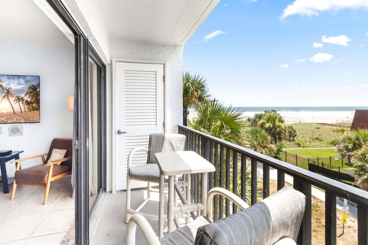 Un balcone con vista sulla spiaggia, una porta, una sedia, un tavolo e un divano.