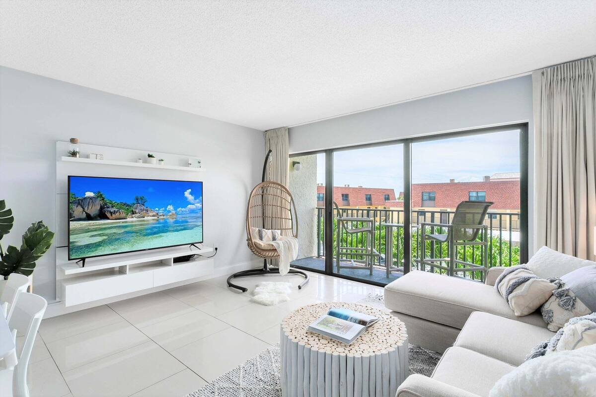Un soggiorno moderno con una TV a schermo piatto, una poltrona in vimini, un divano e un balcone con mobili da esterno.