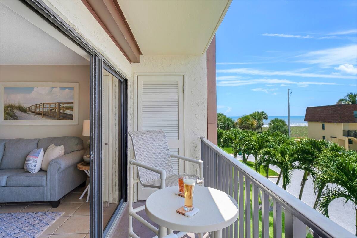 Un balcone con un divano, una sedia, un tavolo e un bicchiere di birra, e un quadro.