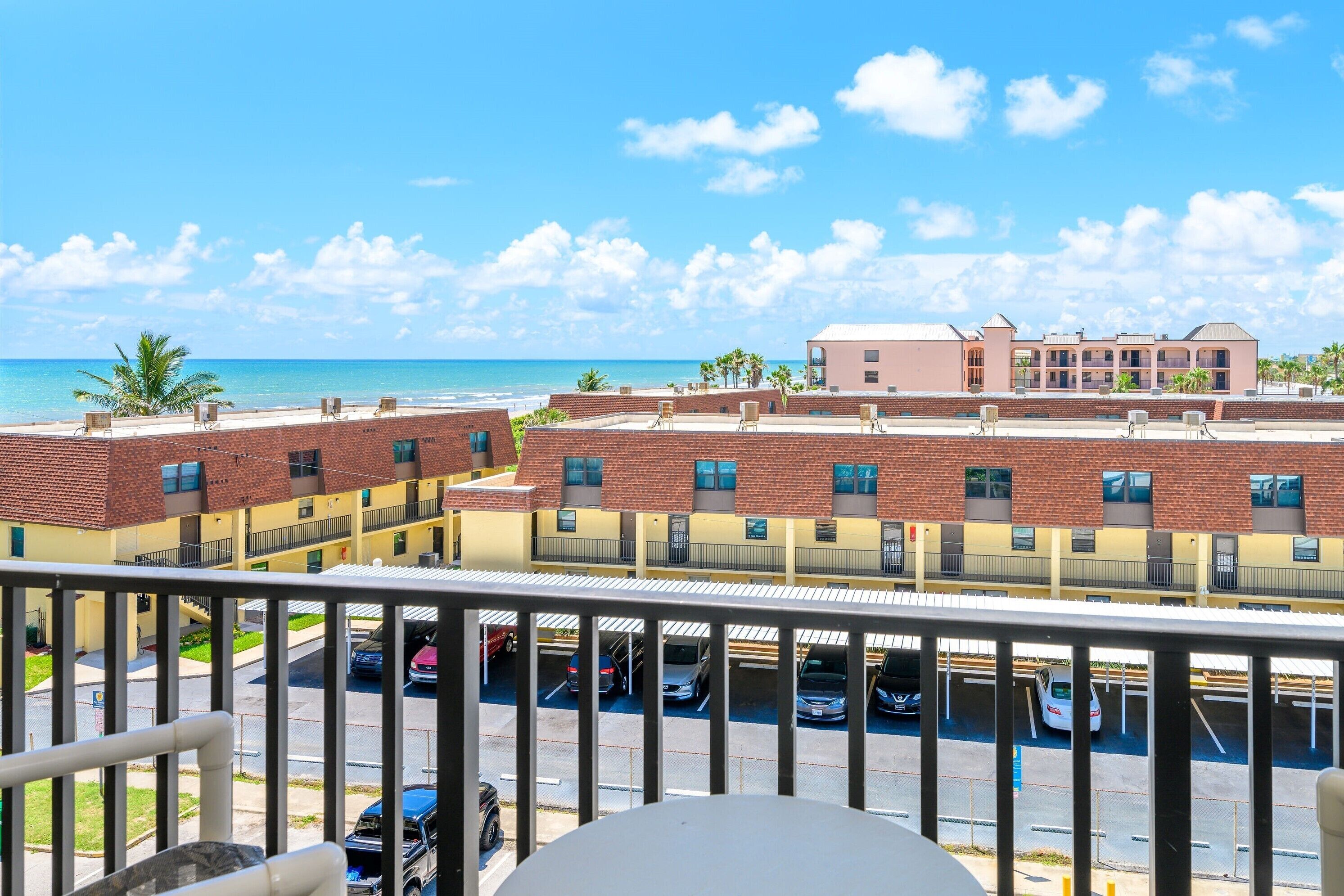 A hotel with a view of the beach, parking, and a fenced balcony.