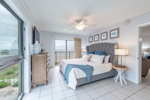 Relax in a spacious room with a large bed, tufted headboard, and multiple pillows. Enjoy a view of the outdoors from the large window.