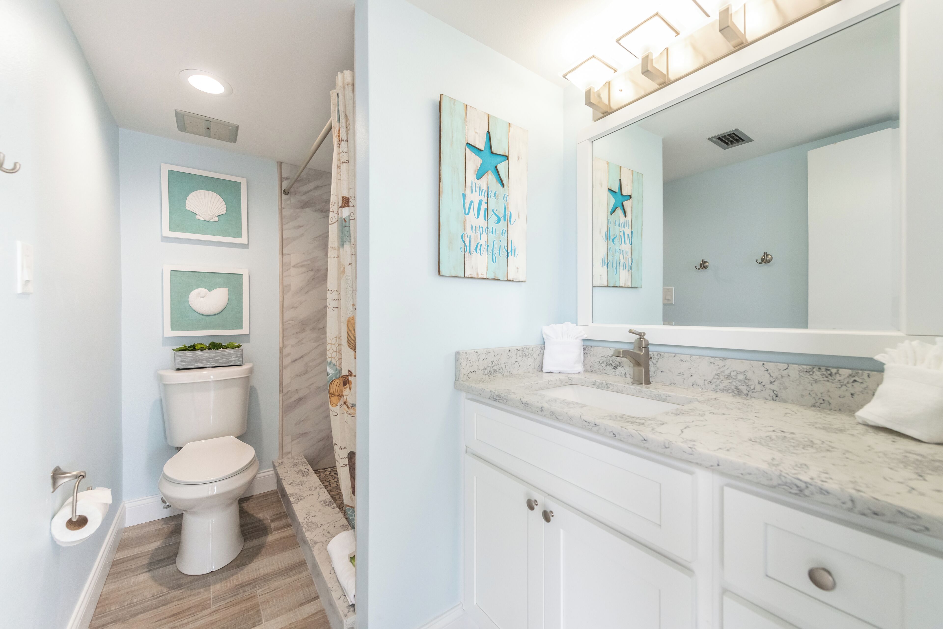 A bathroom with a toilet, sink, and mirror. There are framed pictures on the wall.
