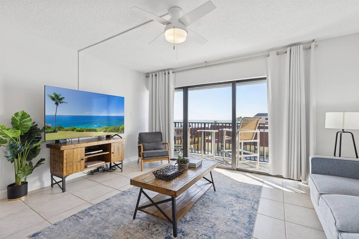 Un soggiorno moderno con un'ampia televisione, un tavolino in legno e un balcone con vista.