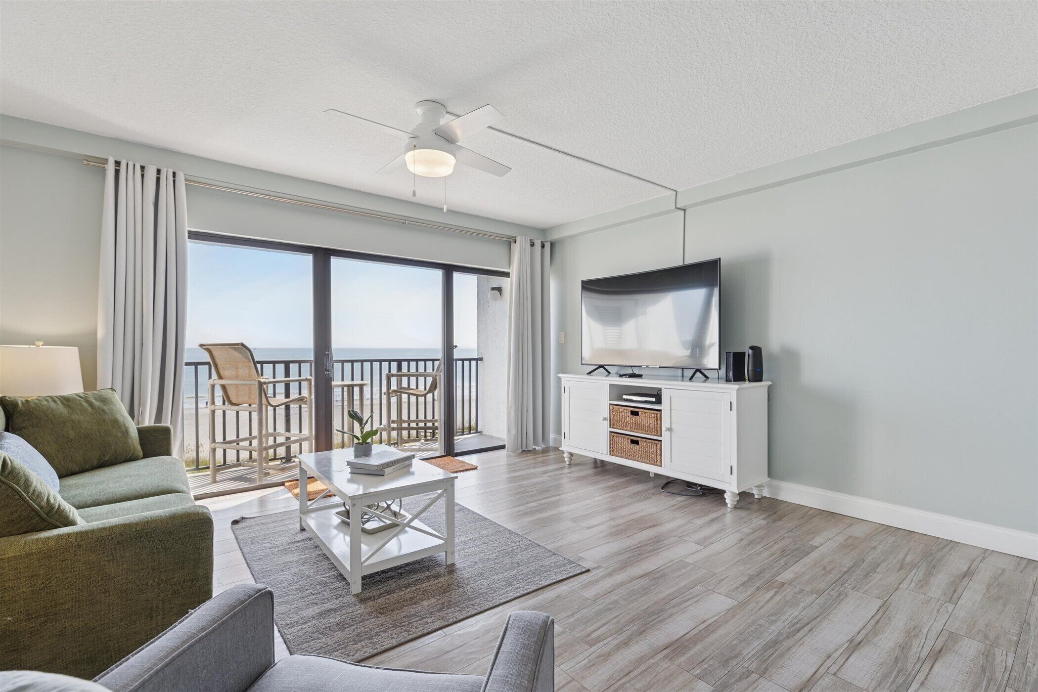 A modern living room with a sofa, coffee table, TV, and a balcony with outdoor furniture.