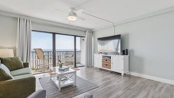 A modern living room with a sofa, coffee table, TV, and a balcony with outdoor furniture.