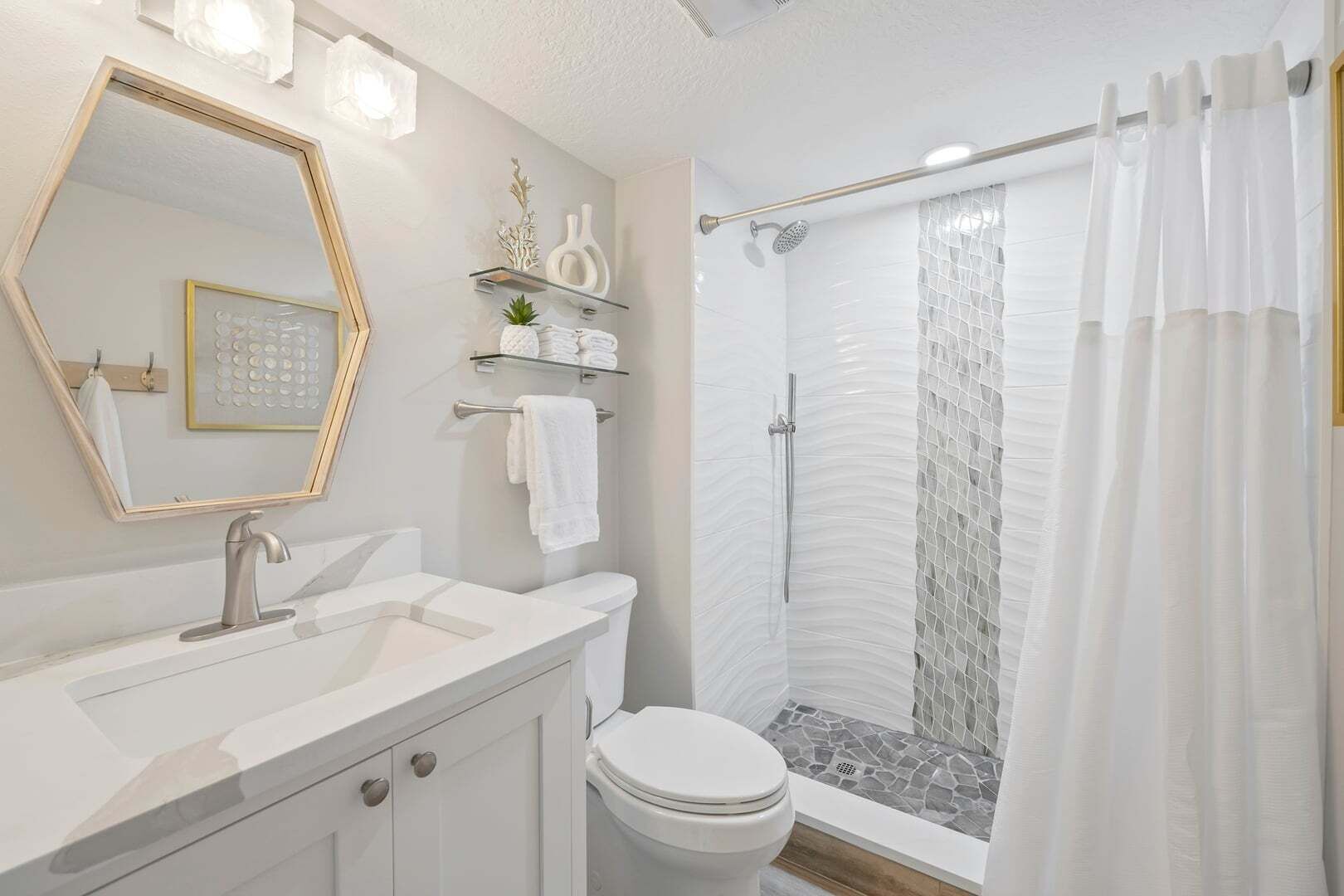 Un baño moderno con tocador, inodoro, ducha con puerta de vidrio y espejo con luces.