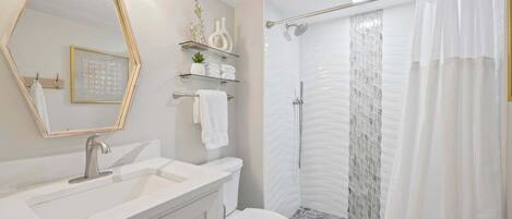 Un baño moderno con tocador, inodoro, ducha con puerta de vidrio y espejo con luces.