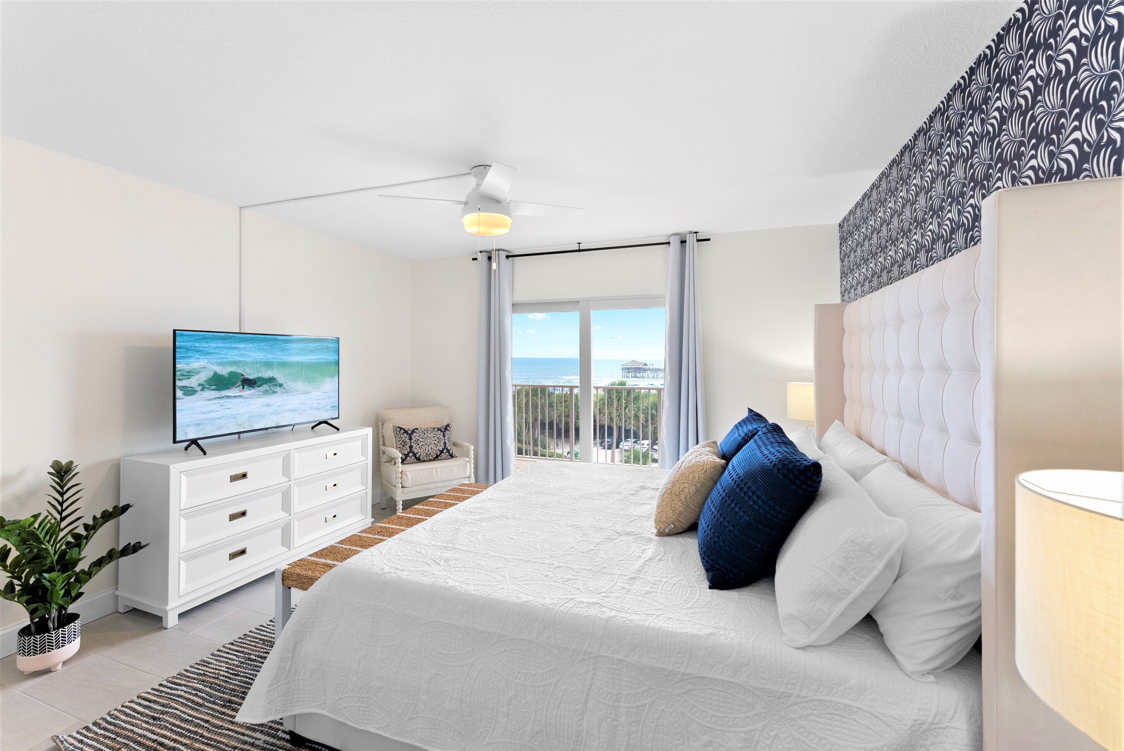 Ein modernes Schlafzimmer mit einem großen Bett, einem Fernseher, einer weißen Kommode und einem Balkon mit Blick.