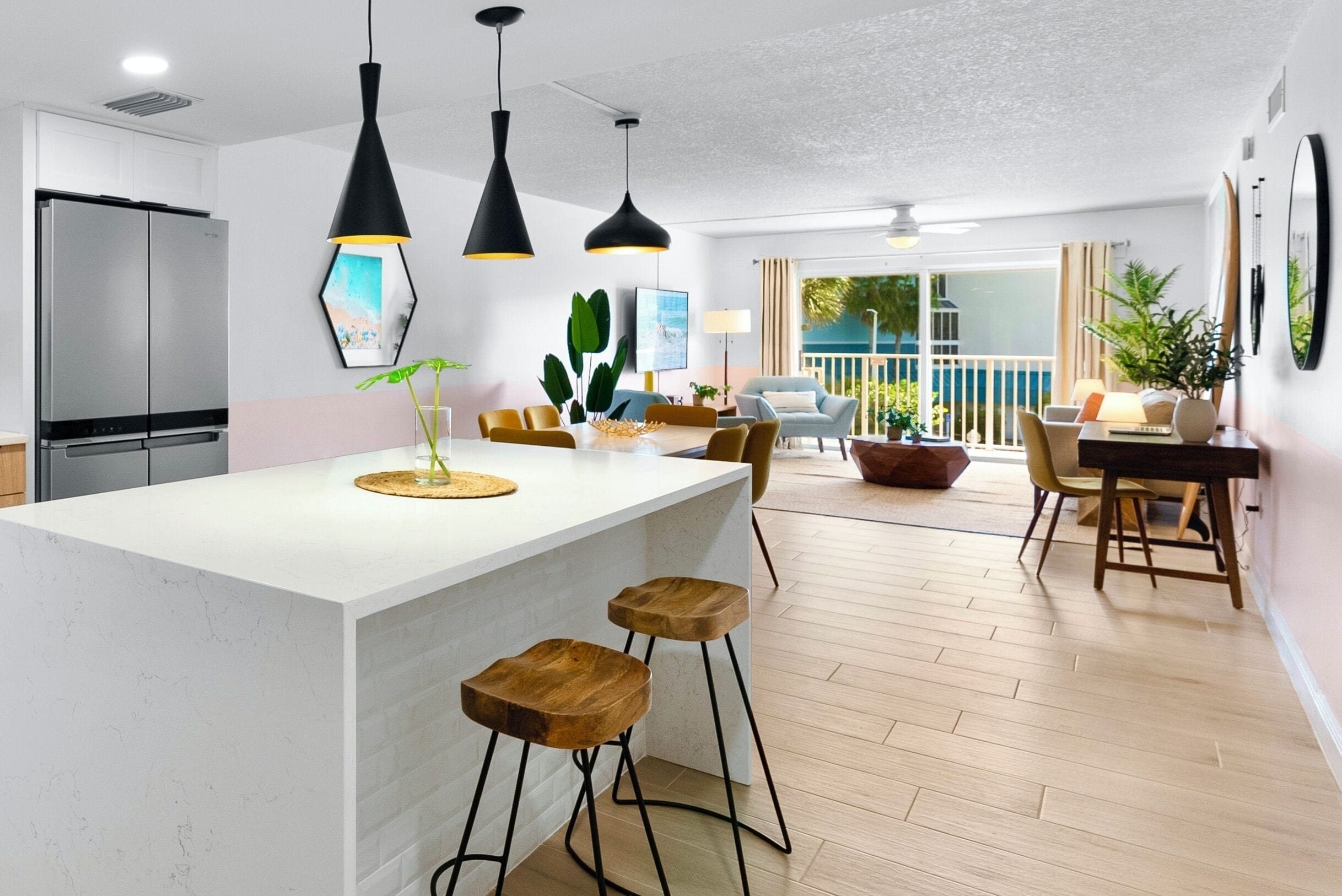 A modern kitchen with a central island, bar stools, pendant lighting, and a dining area with a view.