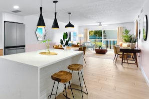 Cozinha moderna com ilha central, banquetas, iluminação pendente e área de refeições com vista.