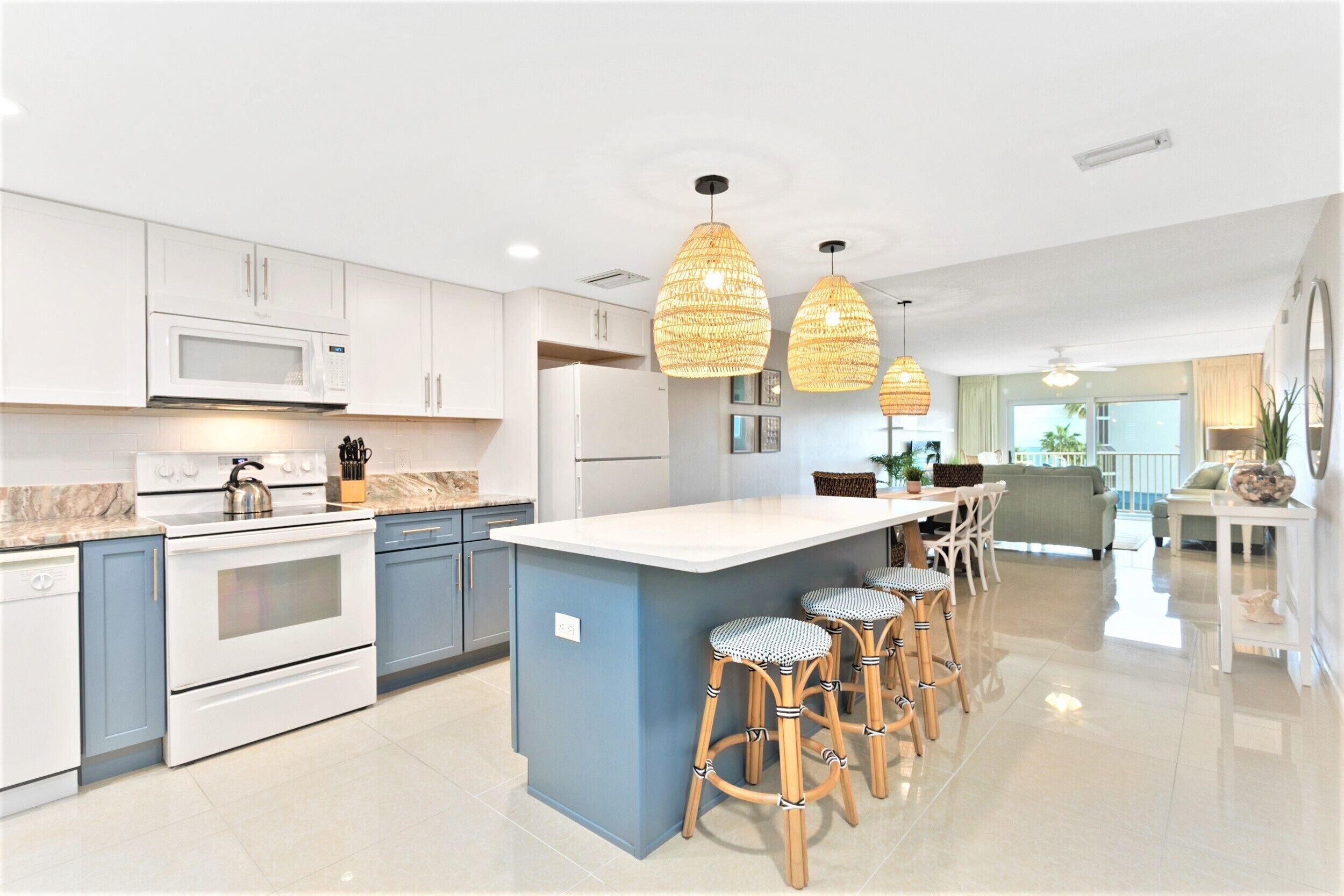 A modern kitchen with white cabinets, a central island with bar stools, and pendant lighting.