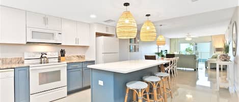 A modern kitchen with white cabinets, a central island with bar stools, and pendant lighting.