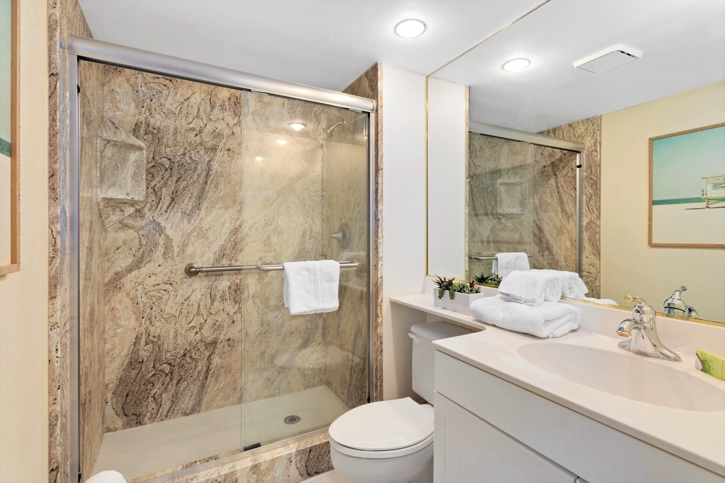 A modern bathroom with a glass-enclosed shower, a white toilet, and a vanity with a sink and mirror.