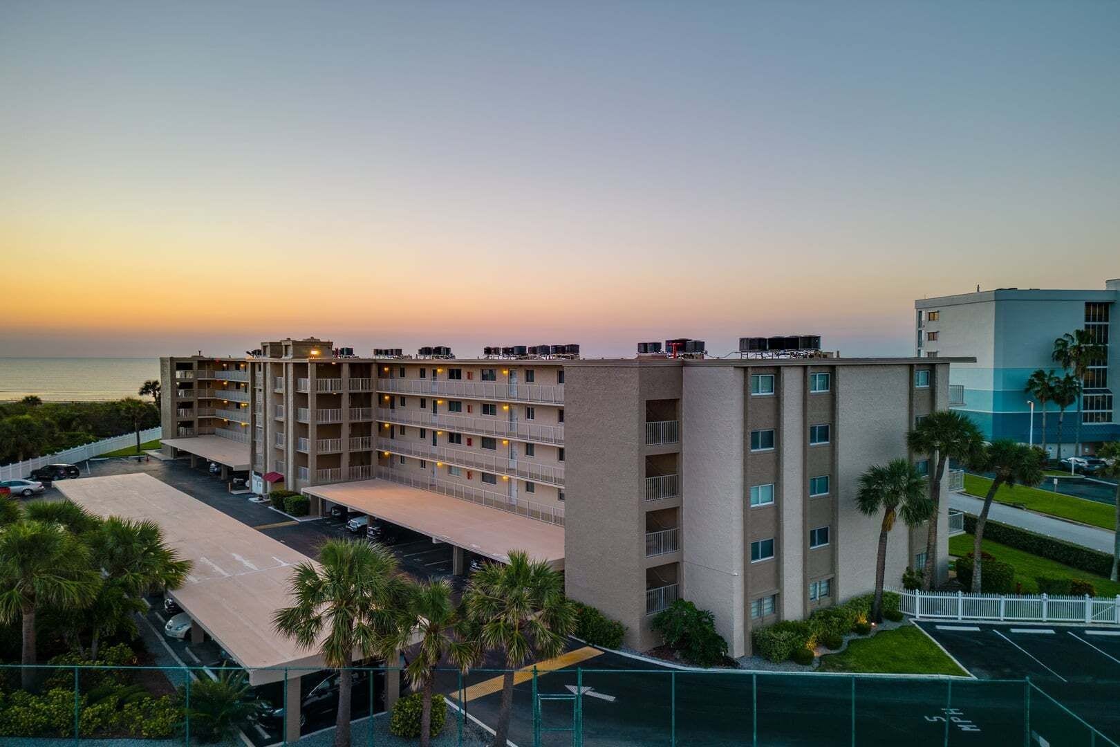 Ein mehrstöckiges Hotel mit Parkplatz und Blick auf den Sonnenuntergang über dem Meer.