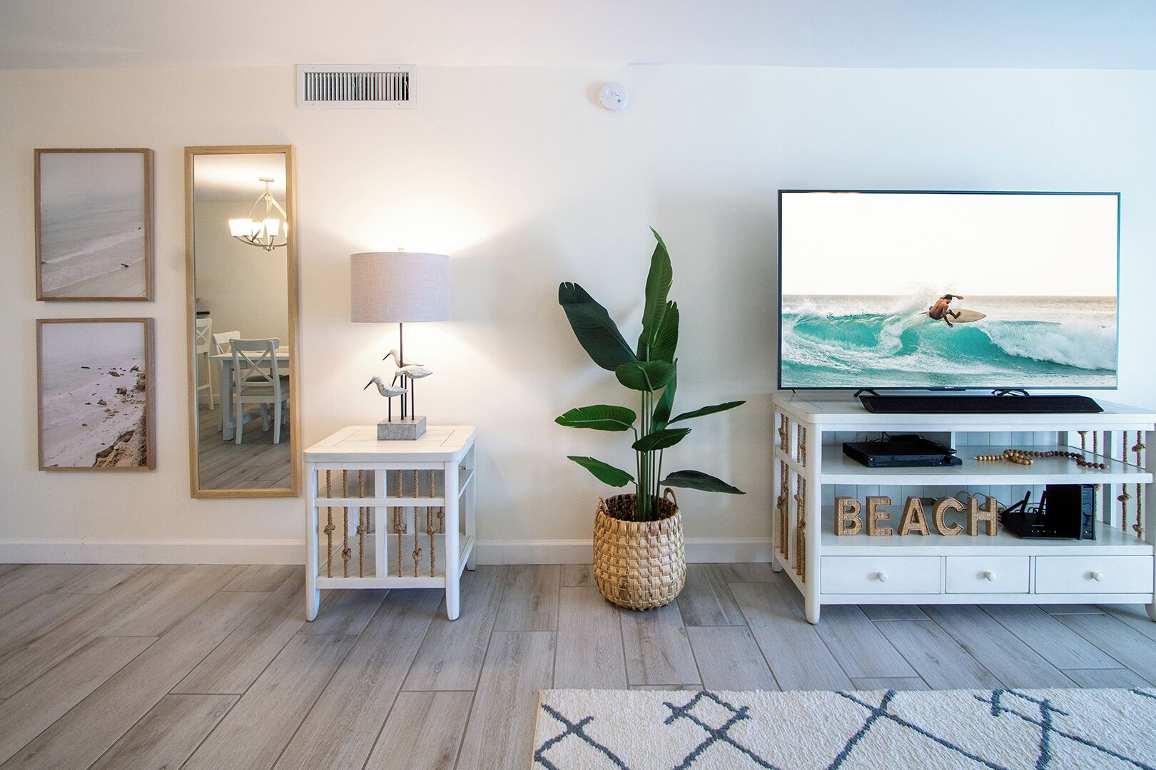 A living room with a TV displaying a surfer, a plant, and artwork on the walls.