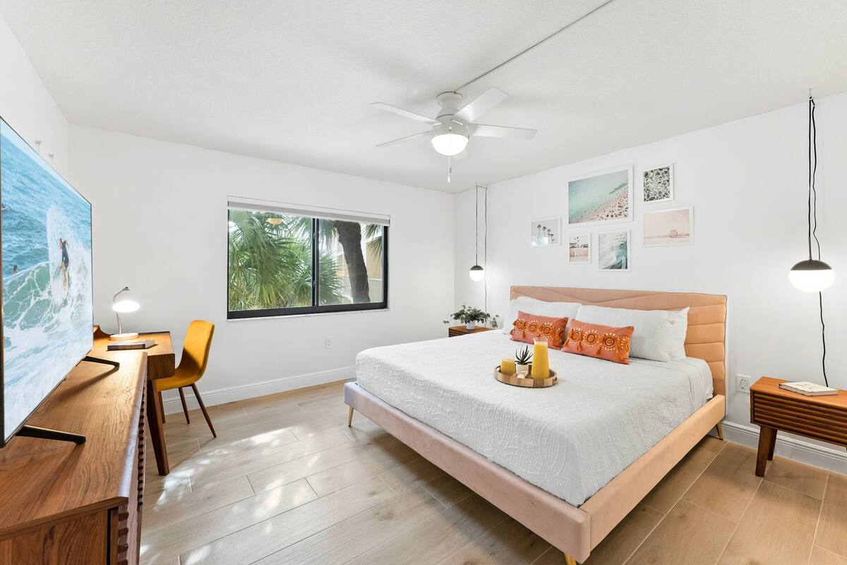 A bedroom with a bed, desk, chair, and a window with a view of trees.