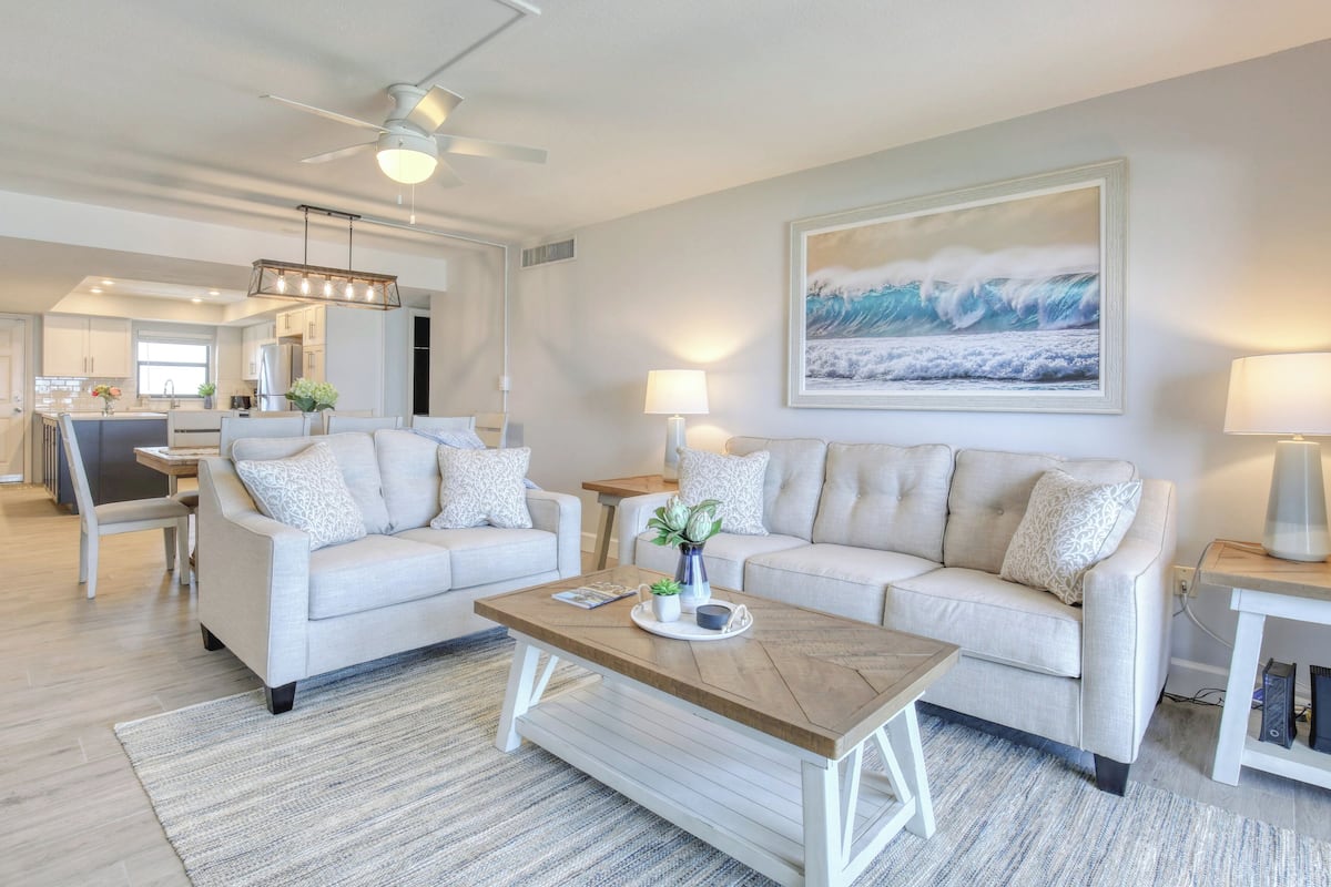 A modern living room with two sofas, a coffee table, and a painting of waves on the wall.