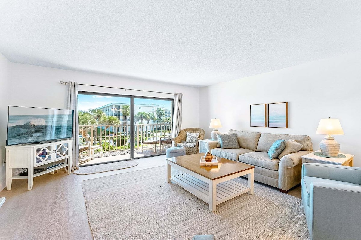 A living room with a TV, sofa, armchair, coffee table, and a balcony with a view.