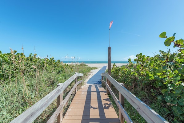 A wooden boardwalk leading to a beach with an American flag on a pole.