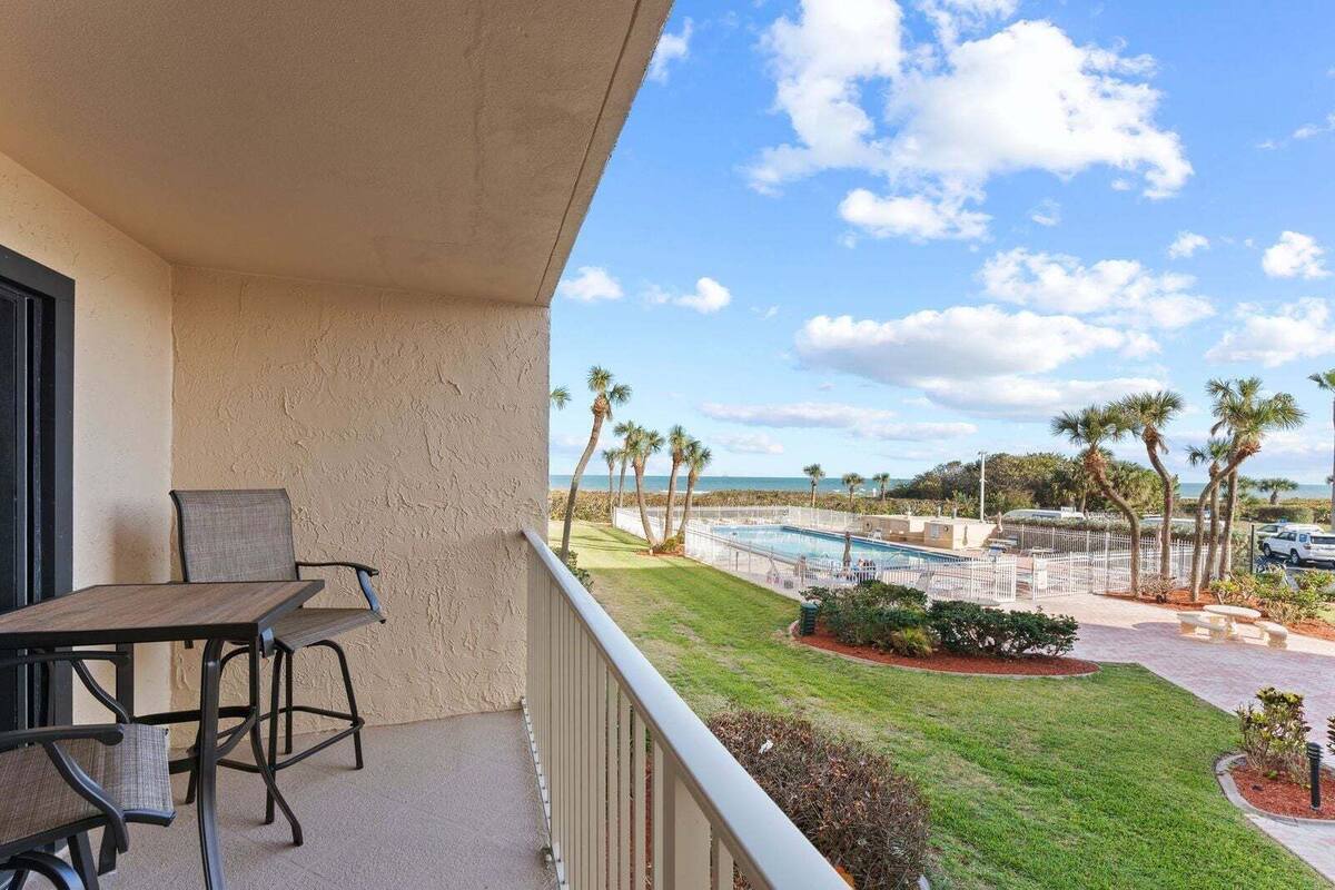A balcony with a table and chairs, overlooking a pool and palm trees.